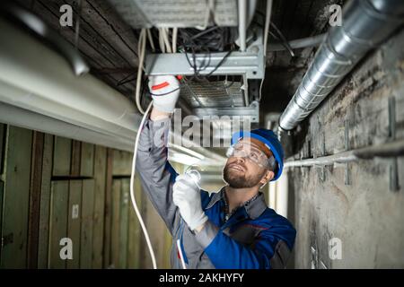 Lavoratore di sesso maschile che indossa il casco di cavi di collegamento Foto Stock