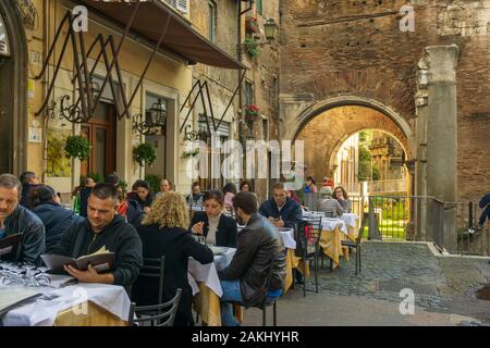 La gente sta mangiando all'aperto in una trattoria tipica in Ghetto, quartiere ebraico di Roma, con Portico di Octavia (Portico di Ottavia) sullo sfondo Foto Stock