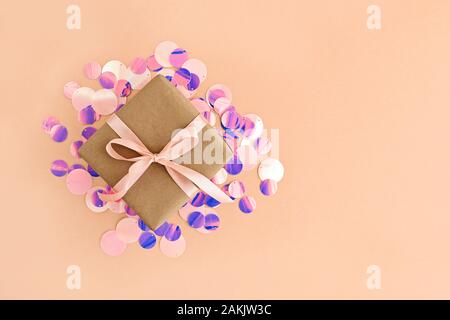 Confezione regalo avvolto in carta artigianale con nastro rosa pallido su sfondo arancione con brillantini. Foto Stock