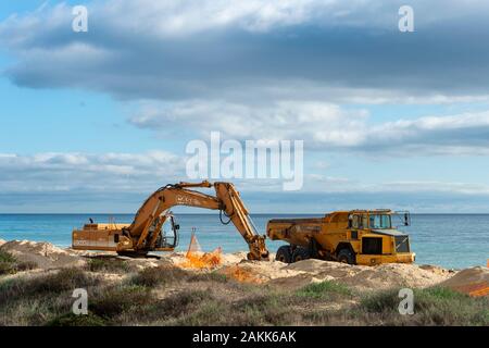 Scavatrice e carrello su una spiaggia di sabbia in movimento per riparare la spiaggia a causa di erosione costiera. Foto Stock