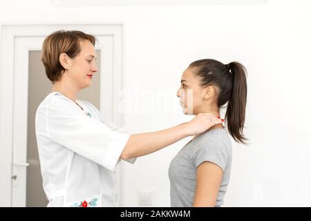 Giovane donna professional a pelo corto terapeuta in un luminoso ufficio medico, esamina un paziente sente la ghiandola tiroide. Foto Stock