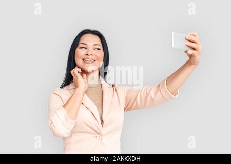 Freestyle. Imprenditrice asiatici in piedi isolato su bianco tenendo selfie sullo smartphone smilign felice Foto Stock