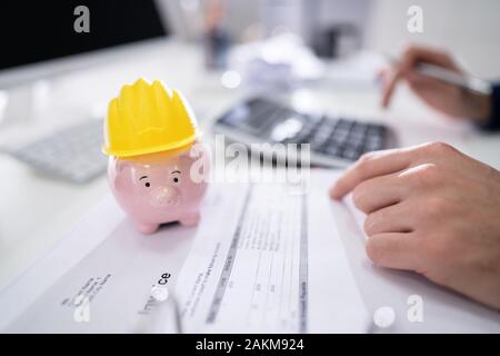 Close-up di Rosa Piggybank con Casco giallo sulla scrivania in legno Foto Stock