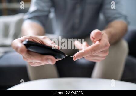 Close-up di una mano di un uomo prova ad alto livello di zucchero nel sangue con il glucometro Foto Stock