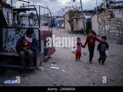 Un uomo palestinese si siede di fronte a casa sua e guarda i suoi figli durante un tempo freddo scrivi in una delle baraccopoli alla periferia di Khan Younis Refugee Camp. Foto Stock