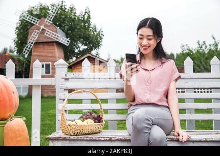 Giovane donna seduta al di fuori del telefono cellulare Foto Stock