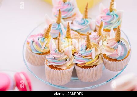 Unicorn fondente glassa tortine con crema di burro color pastello servita sulla lastra trasparente Foto Stock