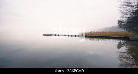 Paesaggio foggy con lago calmo e molo di legno nella tranquilla mattina autunnale in Finlandia Foto Stock