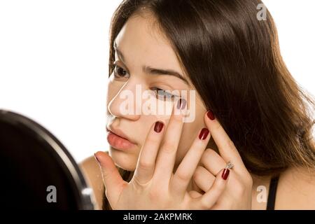 Giovane bella donna applicando il correttore con le dita su sfondo bianco Foto Stock