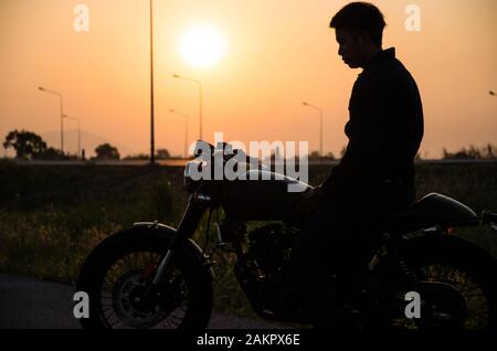 silhouette di uomo equitazione vintage moto caffè stile racer sulla scena del tramonto Foto Stock