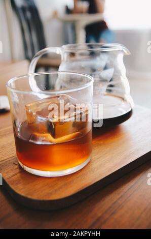 caffè a goccia in vetro con ghiaccio cubico su piastra di legno Foto Stock