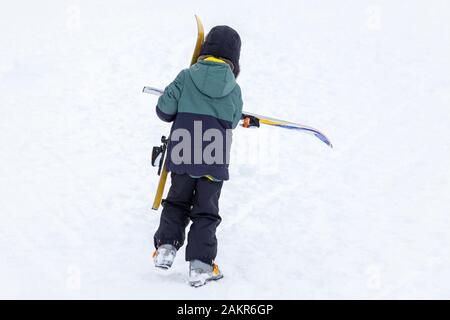 Un ragazzino in abbigliamento invernale va in salita nella neve con gli sci nelle sue mani per imparare a sciare nelle montagne di Altai in inverno. Foto Stock