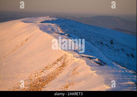 Neve sulla cresta delle montagne in calda luce del sole del sorgere del sole. Foto Stock