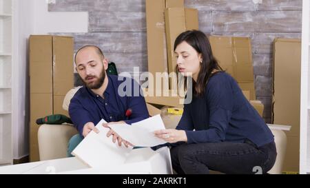 Coppia legge le istruzioni per l'assemblaggio di mobili in casa nuova. Dopo che il lavoro è fatto fanno cinque alto. Foto Stock