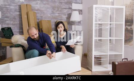 Coppia sorridente durante l'assemblaggio di uno scaffale come una squadra e le istruzioni di lettura. Foto Stock