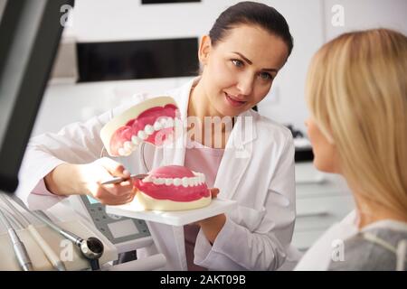 Sorridente dentista che mostra il paziente protesi artificiali Foto Stock