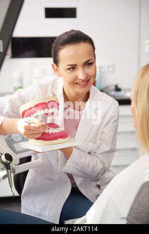 Donna sorridente dentista che mostra il paziente protesi artificiali Foto Stock