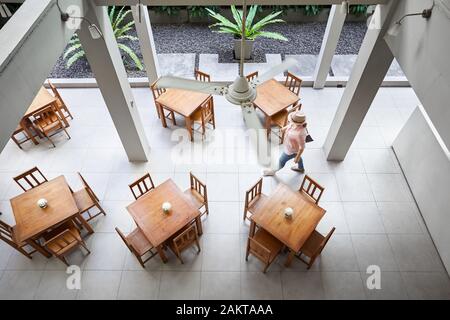 Donna in maglia rosa e hat è camminare vicino a tavola nel ristorante dell'hotel in Bangkok. Vista dall'alto. Foto Stock