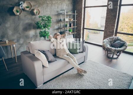 Foto a profilo completo di biondo invecchiato granny buon umore mani dietro la testa guardando soffitto godere nuovo stile casa design seduta comfort divano divano divano divano Foto Stock