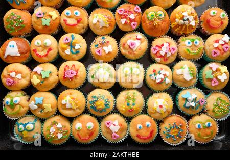 Close-up di un vassoio da forno pieno di piccoli muffin fatti in casa con decorazioni divertenti pronto per una festa di compleanno di bambini Foto Stock
