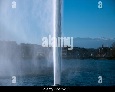 Primo piano dell'iconica e potente fontana a getto d'acqua situata a Ginevra, Svizzera. Il getto d'acqua taglia la foto a metà contro l'acqua blu del lago Foto Stock