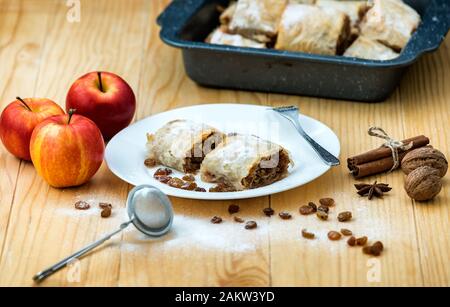 Rotolo di apple pie - Strudel di mele. Torta di mele, cannella, noci e uvetta, spolverati con zucchero a velo in un piatto su un tavolo di legno Foto Stock