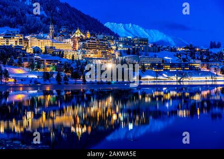 Vista delle belle luci notturne di St. Moritz in Svizzera di notte in inverno, con riflessione dal lago e montagne di neve in backgrouind Foto Stock