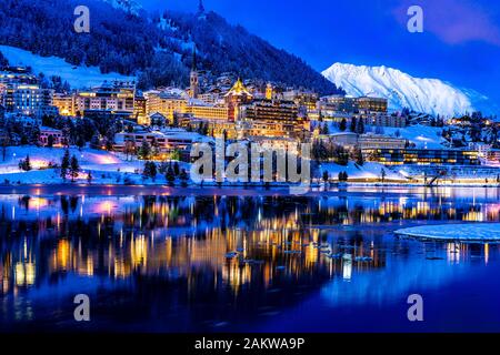 Vista delle belle luci notturne di St. Moritz in Svizzera di notte, con riflesso dal lago e montagne di neve in backgrouind Foto Stock