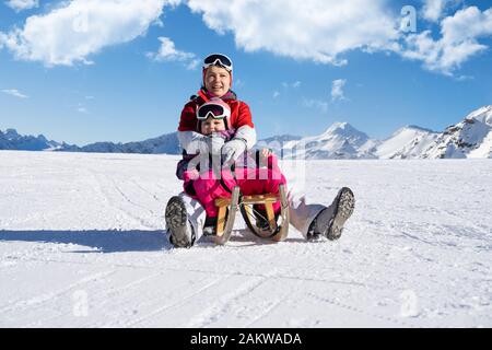 Felice giovane madre e la sua piccola figlia Toddler godendo di un giro in slitta in Winter Park Foto Stock