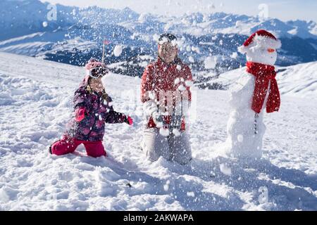 Bella ragazza con sua madre a giocare gettando neve pupazzo di neve vicino a Laax Foto Stock