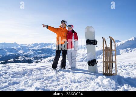 Ritratto di una felice coppia giovane in piedi vicino a Snow Board e slitta di legno nella neve Foto Stock