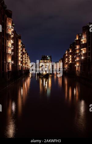 Illuminato Wasserschloss (castello acquatico - famoso edificio storico) nel quartiere Speicherstadt (magazzino) Amburgo dopo il tramonto durante l'ora blu Foto Stock