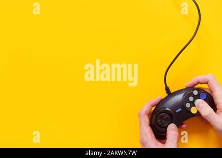 Uomo che tiene il gamepad cablato o il controller di gioco video su sfondo giallo. Vista dall'alto, piatto. Foto Stock