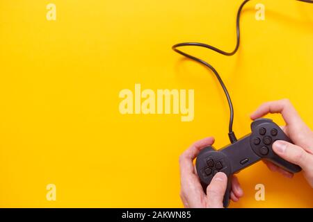 Uomo che tiene il gamepad cablato o il controller di gioco video su sfondo giallo. Vista dall'alto, piatto. Foto Stock