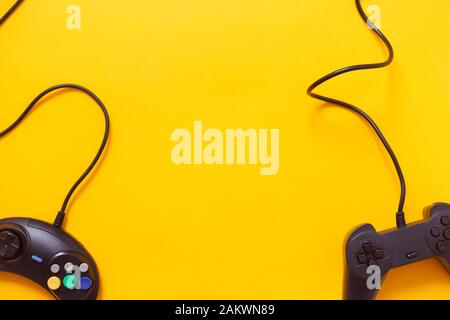 Due gamepad cablati o controller di gioco video su sfondo giallo. Vista dall'alto, piatto. Gaming, settore della console. Foto Stock
