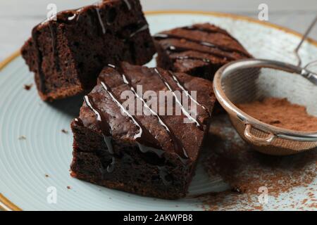 Piastra con fette di torta al cioccolato e filtro con polvere su sfondo di legno, primo piano Foto Stock