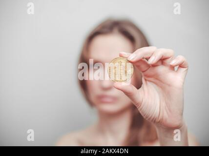 La donna dimostra di tenere una bitcoin in mano su uno sfondo facciale. Foto Stock