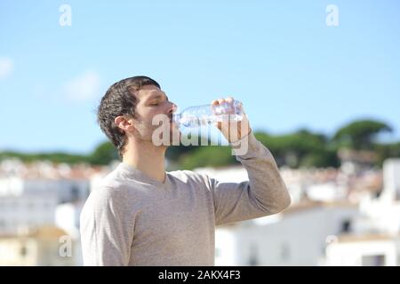 Profilo di un casual uomo adulto di bere acqua in bottiglia in piedi in una città in una giornata di sole Foto Stock