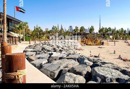 Dubai / Emirati Arabi Uniti - 20 dicembre 2019: La Mer Spiaggia di Dubai. Nuova moderna pubblica spiaggia urbana con bella città sullo sfondo. La Mer a piedi wuth bandiera DEGLI EMIRATI ARABI UNITI Foto Stock