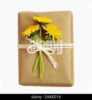 Pacchetto avvolto in carta kraft e legato con una corda e fiori di dandelion isolato su bianco Foto Stock