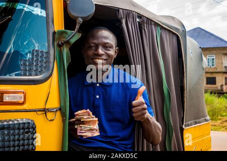 giovane uomo africano che guida un taxi risciò contando i suoi soldi sorridendo dando un pollice in su Foto Stock