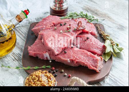 I pezzi di carne sono pronti per la marinata in Dijon senape di grano francese, adagiata su una tavola di argilla con spezie-foglia di baia, pepe, erbe provenzali e olive Foto Stock