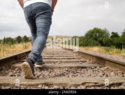 Giovane uomo irriconoscibile che cammina sulle rotaie in una scena rurale in una giornata torbida. Tandil, Buenos Aires, Argentina. Foto Stock