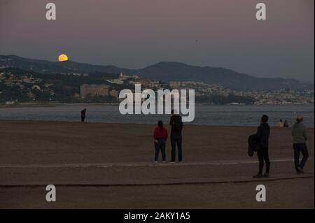 Malaga, Spagna. Decimo gen, 2020. La gente guarda la luna piena (noto come in questo mese come 'Wolf moon") come sorge oltre l'orizzonte in spiaggia durante il primo Eclissi lunare parziale dell'anno. In questo anno 2020 avrà sei eclissi, compreso un eclisse solare totale. Credito: Gesù Merida/SOPA Immagini/ZUMA filo/Alamy Live News Foto Stock