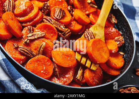 Patate dolci candite con zucchero di canna, sciroppo d'acero, succo d'arancia e noci pecan in una padella con spatola in legno, vista orizzontale dall'alto, chiuso- Foto Stock