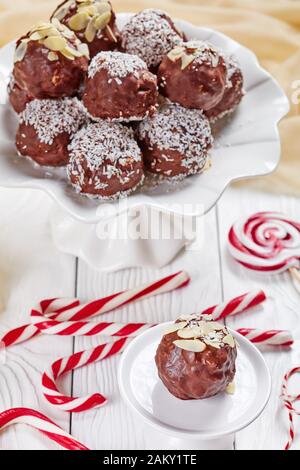 Palline di mandorle di cocco al cioccolato su una base per torte con caramelle su un tavolo di legno, vista verticale dall'alto, primo piano, Foto Stock