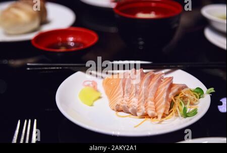 Sashimi di salmone giapponese Focalizzato selettivo (carne di salmone grasso fresco) decorato con rapa grattugiata e carota in piatto bianco su sfondo tabella di marmo. Foto Stock