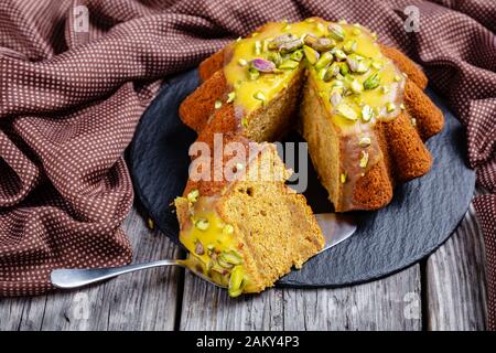 pan di spagna di zucca con glassa di arancia, cosparsa di pistacchi su una piastra nera su un rustico tavolo di legno, primo piano Foto Stock