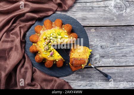 primo piano di pan di spagna di zucca affettata con glassa d'arancia, cosparsa di pistacchi su un piatto nero su un rustico tavolo di legno, piatto, piatto libero sp Foto Stock