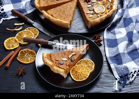 Torta di patate dolce a fette decorata con patatine arancioni, semi di zucca e stelle anice su un piatto nero su un tavolo di legno, vista orizzontale dall'alto, clo Foto Stock